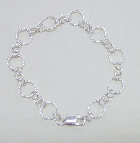 A silver round link bracelet with hammered or polished finish, featuring a large hammered link and three small links and a lobster clasp.