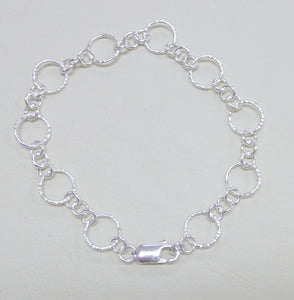 A silver round link bracelet with hammered or polished finish, featuring a large hammered link and three small links and a lobster clasp.