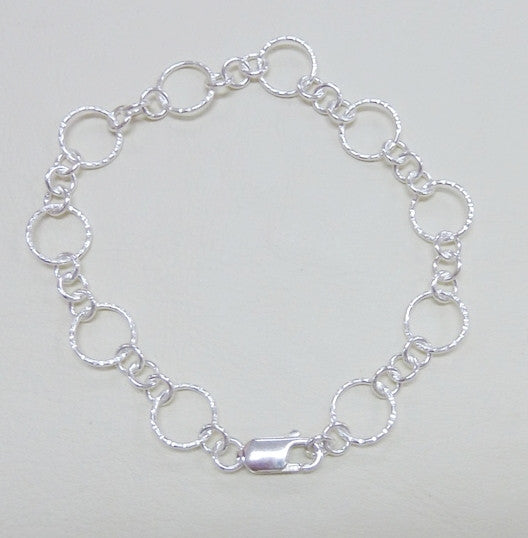 A silver round link bracelet with hammered or polished finish, featuring a large hammered link and three small links and a lobster clasp.